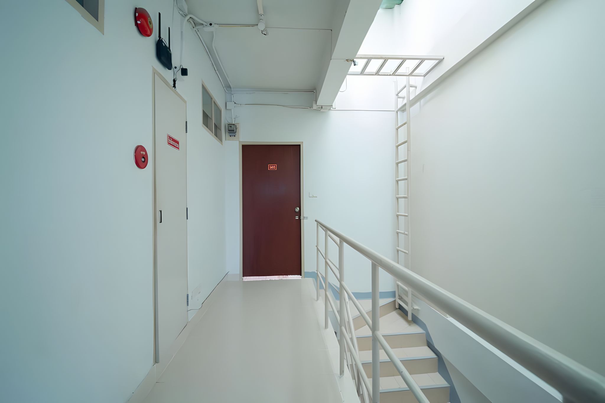 A hospital corridor with a staircase, emergency exit signs, and a door at the end.