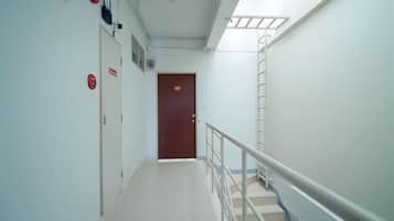 A hospital corridor with a staircase, emergency exit signs, and a door at the end.