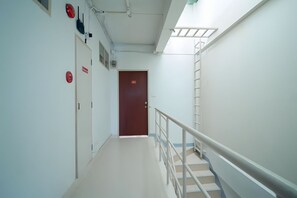 Un pasillo de hospital con una escalera, señales de salida de emergencia y una puerta al final.