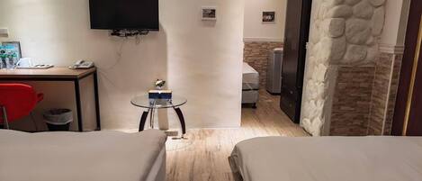 Habitación de hotel con dos camas, un escritorio con silla, una mesita, televisor montado en la pared y una pared de acento de piedra.