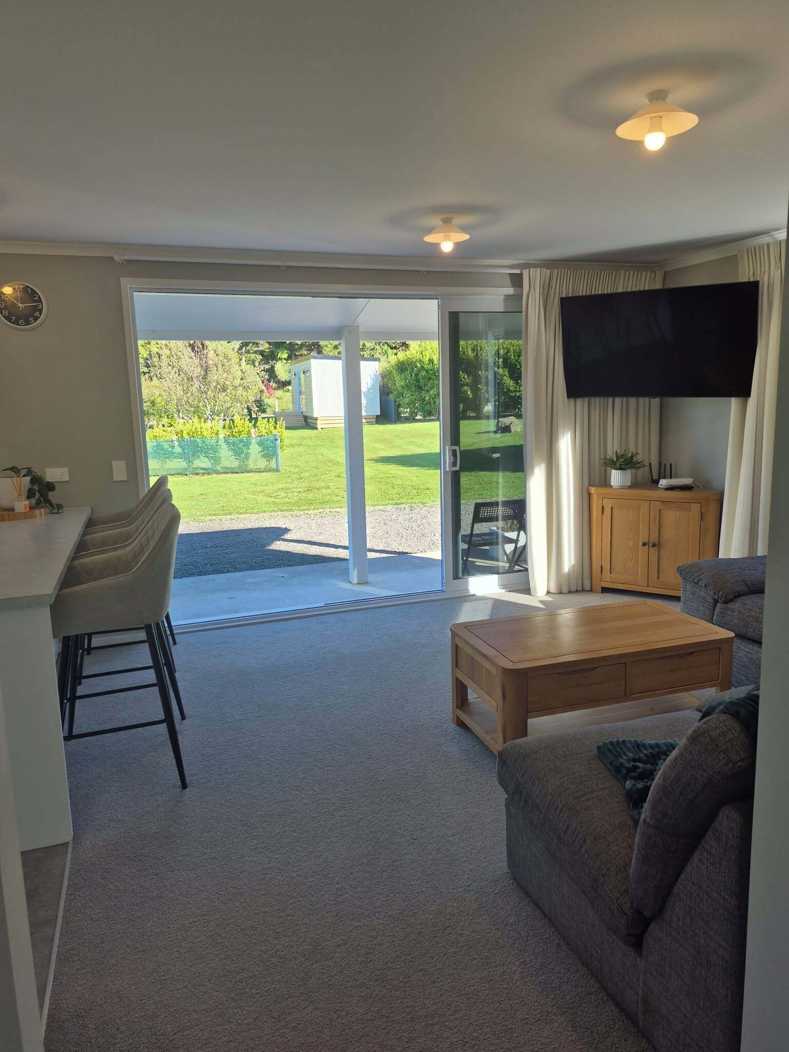 A living room with a sofa, coffee table, TV, and a sliding glass door leading to a garden.