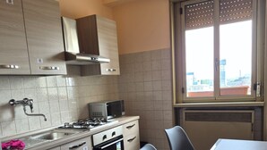 A compact kitchen with a gas stove, microwave, and oven, a window with blinds, and a dining area with a table and chairs. - Venice Nice apartment (Venezia)