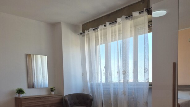 A hotel room with two beds, a chair, a dresser, a mirror, and a window with sheer curtains. - Venice Nice apartment (Venezia)