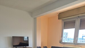 A modern living room with a sofa, a TV on a wooden cabinet, and a window with blinds. - Venice Nice apartment (Venezia)