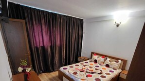 Un dormitorio con cama, una mesita de noche de madera, un escritorio, una silla, un armario y una cortina.