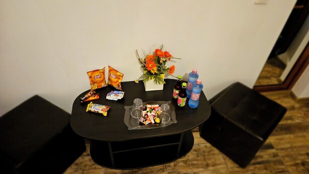 Una pequeña mesa con aperitivos, bebidas y un arreglo floral.