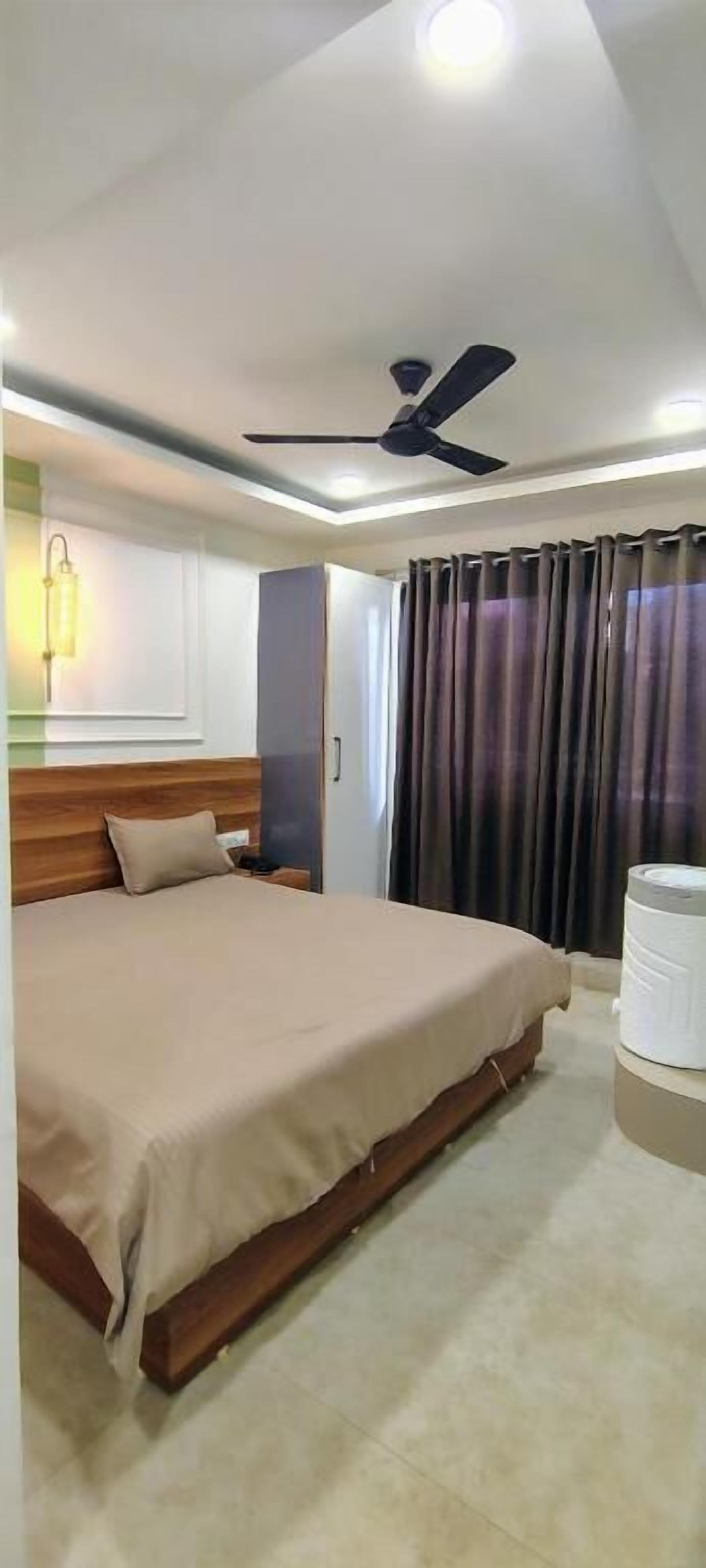 A hotel room with a bed, a ceiling fan, a nightstand, a lamp, and a window with curtains.