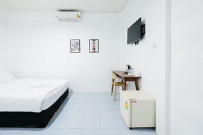 Een minimalistisch hotelkamer met een bed, een bureau, een stoel, een televisie en een airconditioner.