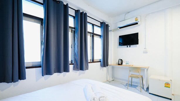 Una habitación de hotel con cama, escritorio, silla, televisor y ventana con cortinas.