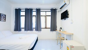 Una habitación de hotel con cama, escritorio, televisión y ventana con cortinas.
