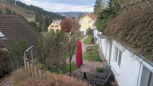 A residential area with a paved pathway, a small patio with a table and chairs, and a red umbrella. - Sonneck vacation apartment for 4 people with direct access to the garden. (Feldberg (Schwarzwald))