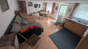 A living room with a sofa, a dining table, and a kitchen area with a sink and cabinets. - Sonneck vacation apartment for 4 people with direct access to the garden. (Feldberg (Schwarzwald))
