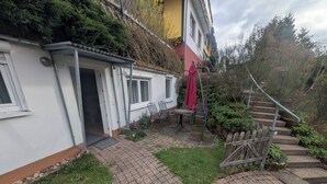 A residential building with a paved patio, a wooden fence, and a staircase leading up to a higher level. - Sonneck vacation apartment for 4 people with direct access to the garden. (Feldberg (Schwarzwald))