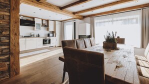 A spacious living area with a wooden dining table, a sofa, and a kitchen in the background. - Chalet Molly, garden & sauna (Zell am See)