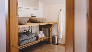 A bathroom with a wooden vanity, a stone basin, towels, and a trash can. - Chalet Molly, garden & sauna (Zell am See)