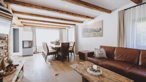 A cozy living room with a wooden ceiling, a brown leather sofa, a wooden coffee table, and a dining area with a table and chairs. - Chalet Molly, garden & sauna (Zell am See)