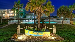 Une vue nocturne d’un complexe hôtelier avec une piscine, des palmiers et un panneau indiquant « Island Retreat ».