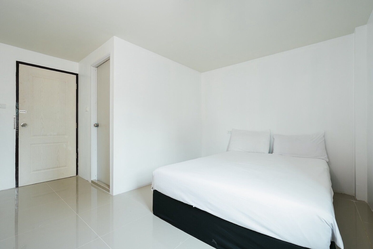 Un dormitorio con cama, una puerta y pared blanca.