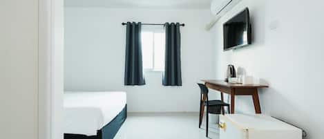 A room with a bed, a desk, a chair, a TV, and an air conditioning unit.