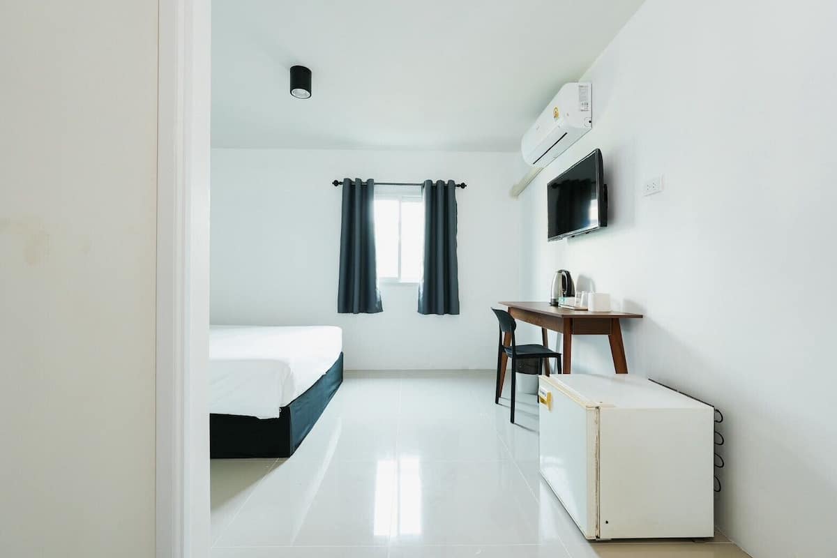 Una habitación de hotel con cama, escritorio, silla, televisor y aire acondicionado.