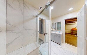 Ein modernes Badezimmer mit Duschkabine aus Glas, Wandverkleidung aus weißem Marmor und Holzboden.