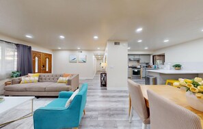 A modern living room with a sofa, a teal armchair, and a dining area with a table and chairs. - Gorgeous 4-bedroom house with Hot Tub in Huntington Beach I 31 nights + (Huntington Beach)