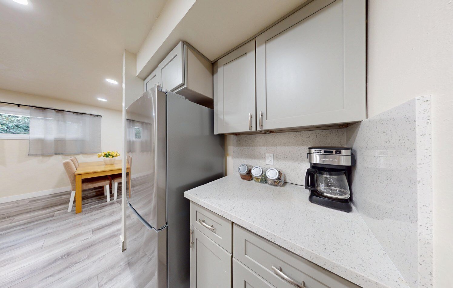 Una cocina compacta con un refrigerador, una cafetera y frascos en la encimera.