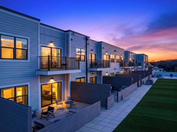 Un moderno edificio residencial de varios pisos con balcones, mobiliario exterior y un césped bien cuidado.
