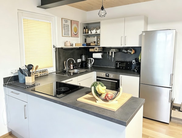 A modern kitchen with a built-in oven, a refrigerator, and a countertop with a fruit bowl.