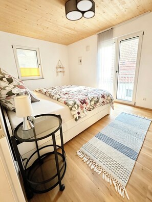 Une chambre à coucher avec un lit, une table de chevet avec une lampe, une fenêtre et une porte.