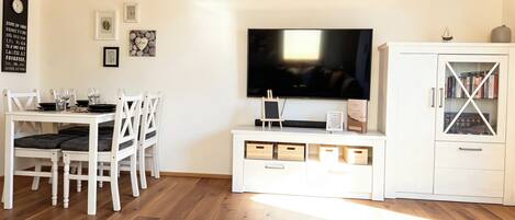 A living room with a TV, white furniture, and a cabinet with books.