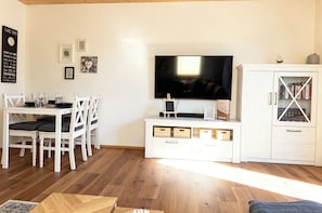 A living room with a TV, white furniture, and a cabinet with books.