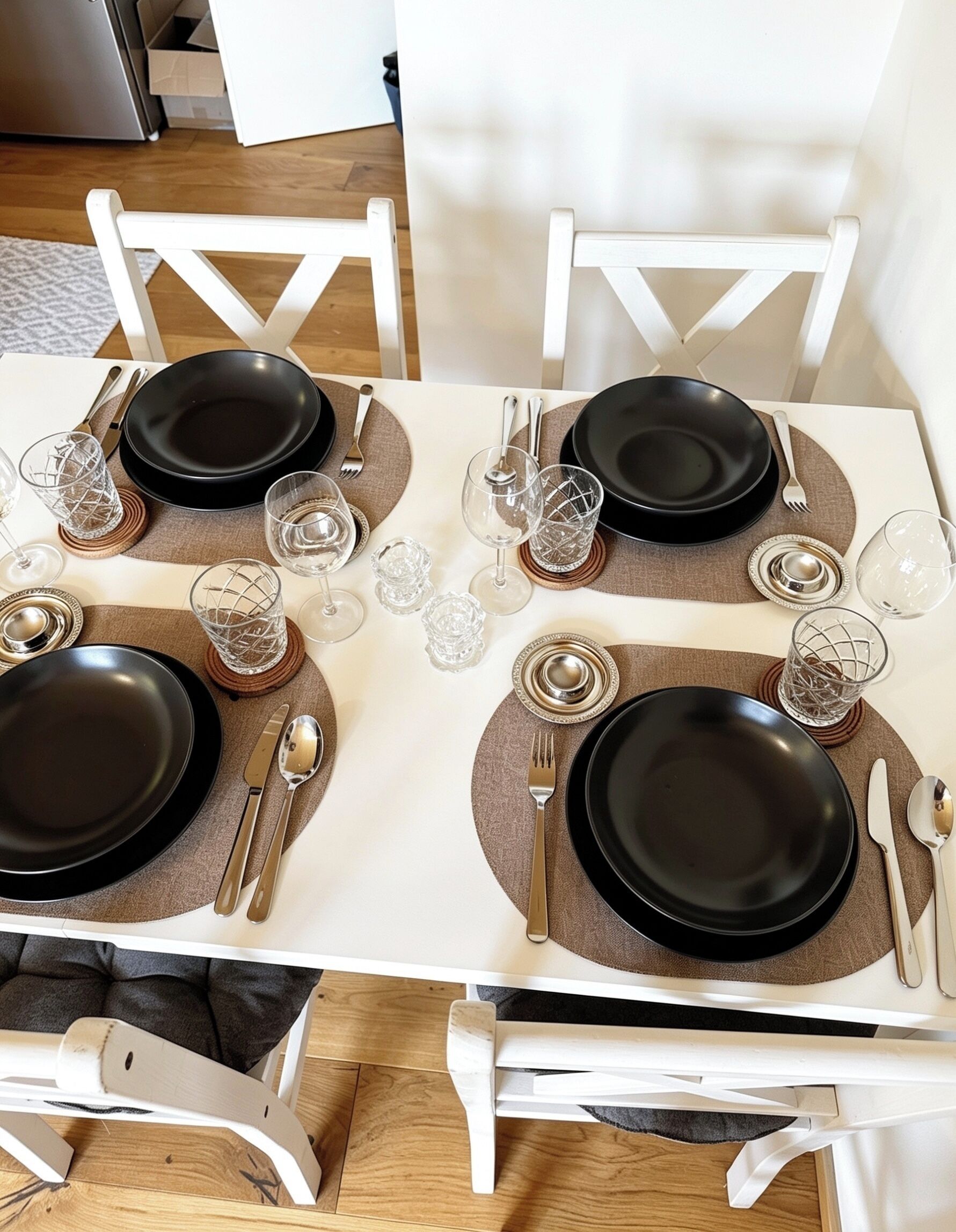 A dining table set for four with black plates, silverware, and clear glassware.