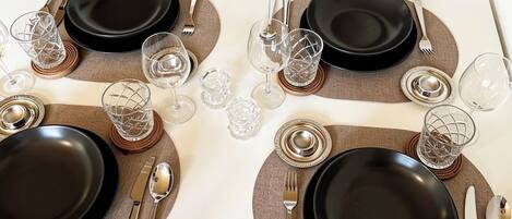 A dining table set for four with black plates, silverware, and clear glassware.