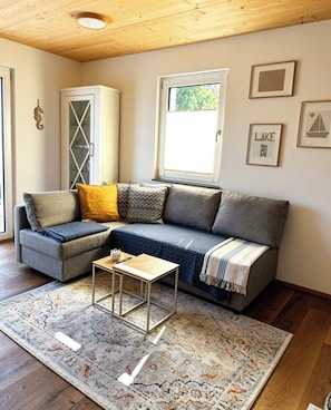 Un salon chaleureux avec un canapé d’angle, une petite table, un tapis à motifs et une fenêtre donnant sur un beau paysage.