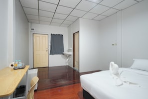 A hotel room with a wooden desk, a bed with white linens, a bathroom with a sink, and a shower curtain. - AT Pranakorn (Bangkok)