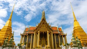 Een tempel met een centrale ingang, geflankeerd door twee gouden torens, onder een gedeeltelijk bewolkte lucht.