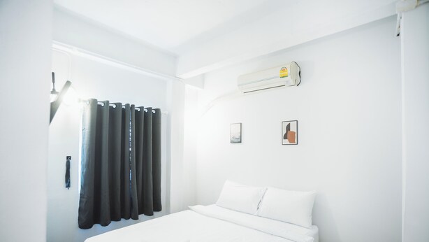 A hotel room with a bed, an air conditioning unit, a window with curtains, and a wall-mounted light fixture. - AT Pranakorn (Bangkok)