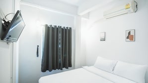 A hotel room with a bed, a flat-screen TV, a window with curtains, and an air conditioning unit. - AT Pranakorn (Bangkok)