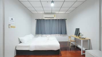 A hotel room with a bed, a desk with a chair, an air conditioning unit, and a small refrigerator.