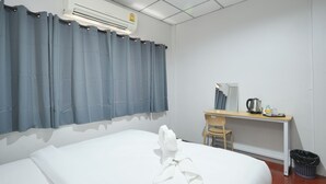 Een hotelkamer met een bed, een bureau met stoel, een airconditioner en een prullenbak.