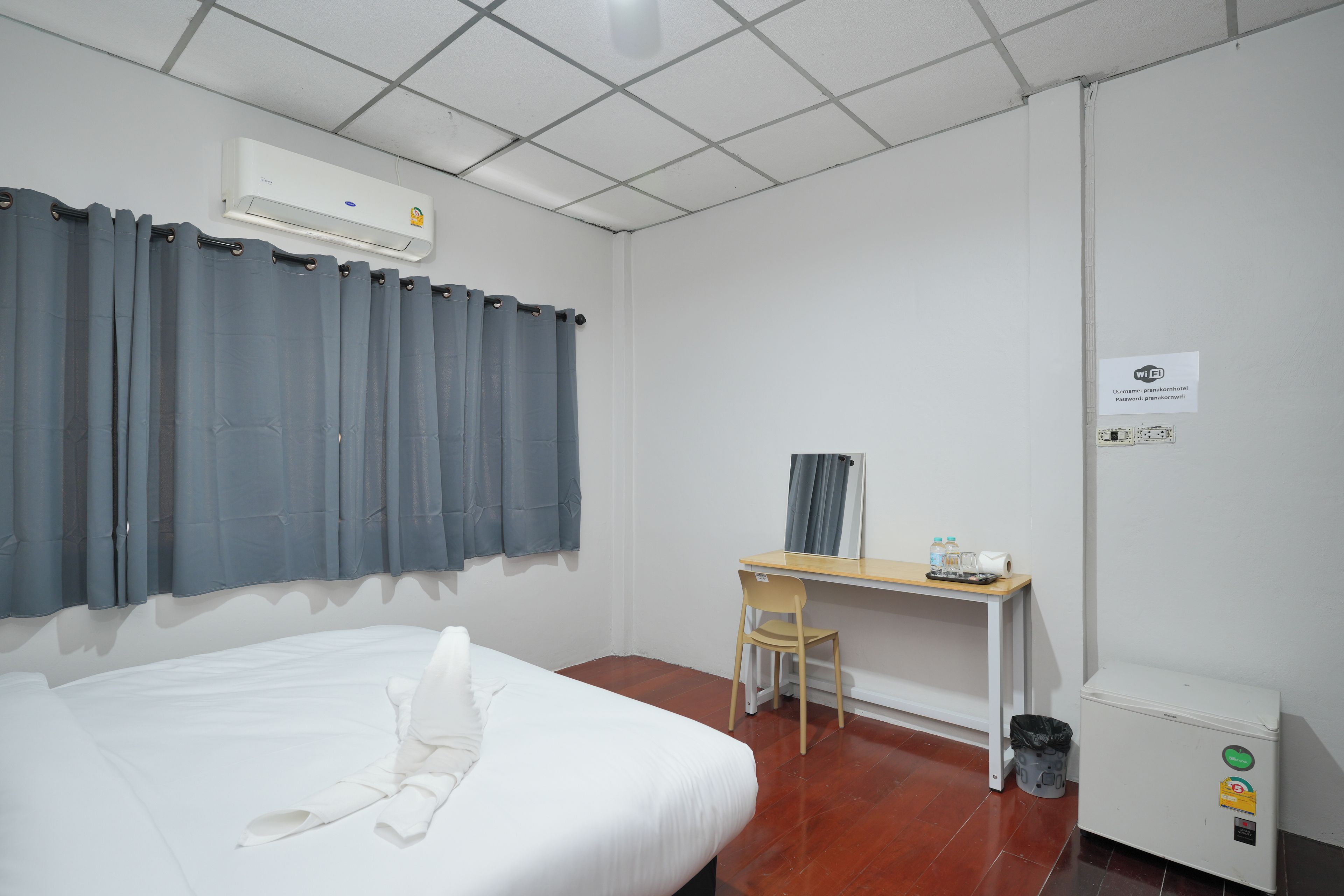 Habitación de hotel con cama, escritorio, silla, aire acondicionado, cubo de basura y un cartel que indica acceso a Wi-Fi.