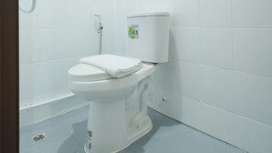 Een kleine, witte badkamer met toilet, douche en een raam.