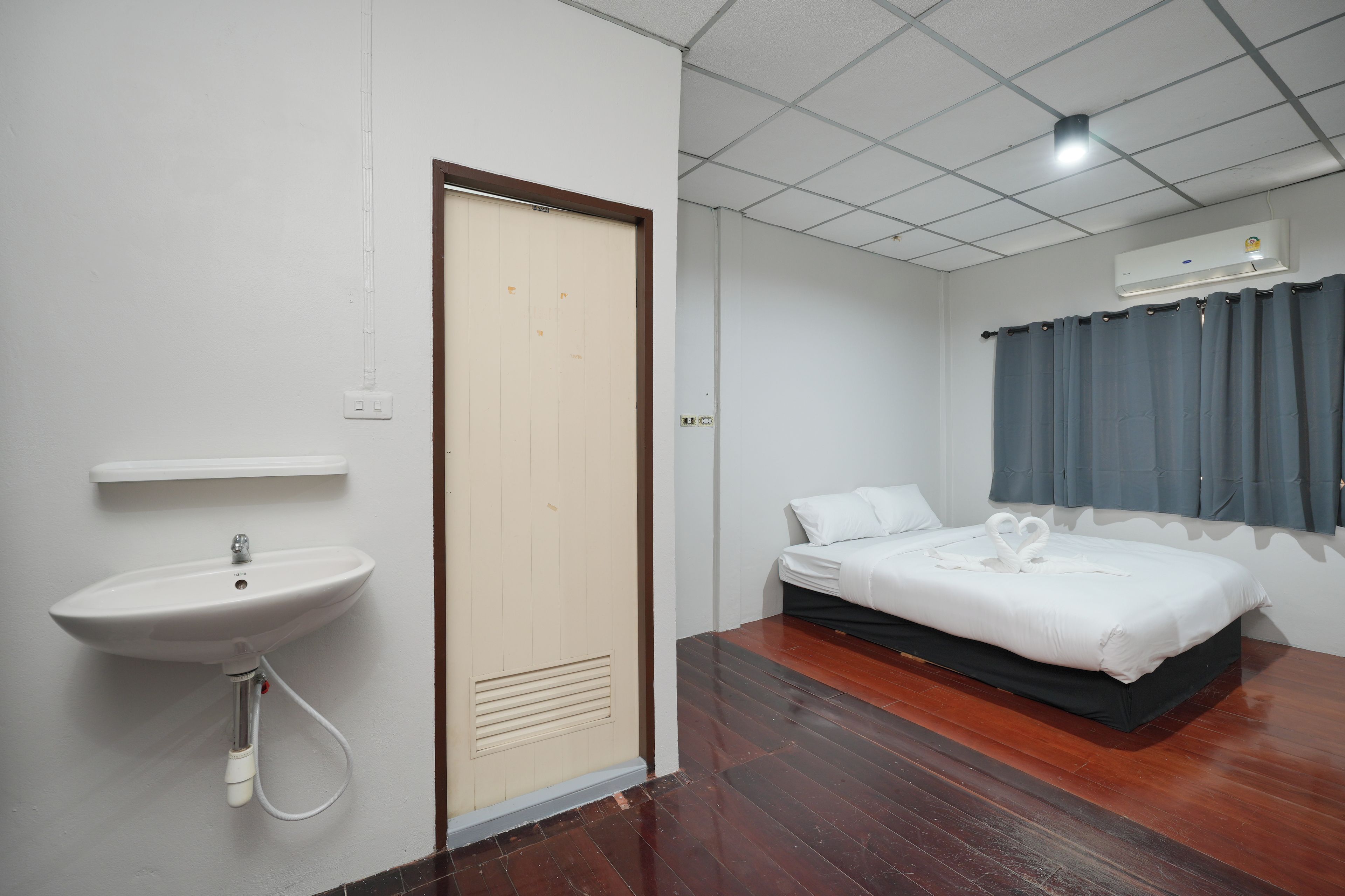 A hotel room with a bed, a bedside table, a wall-mounted sink, and a door.