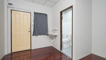 A narrow hallway with a wooden floor, a beige door, a grey curtain, a white sink, and a toilet.
