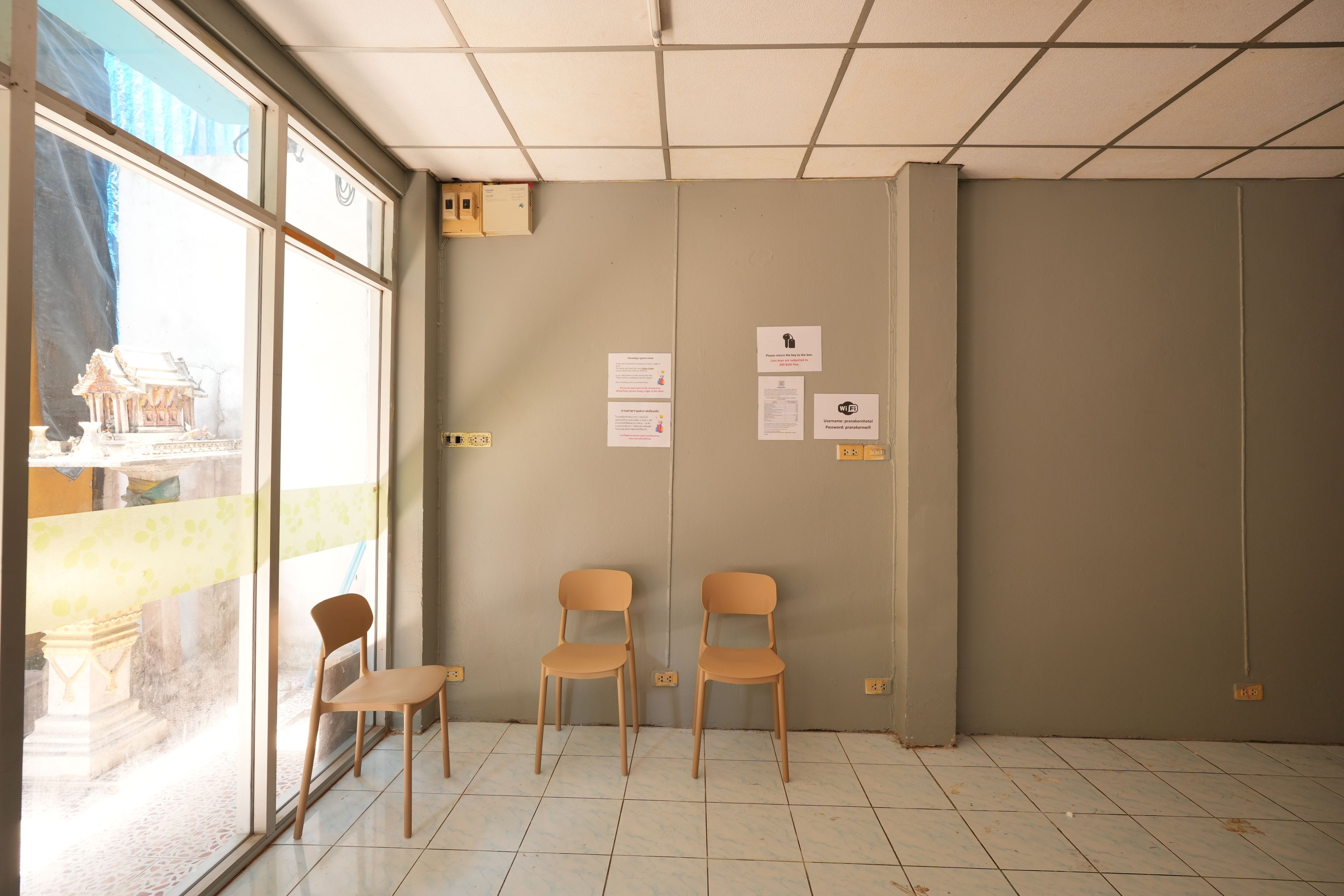 Un área de espera con dos sillas, una ventana que ofrece vista a un edificio y una puerta con un letrero.