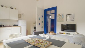 Ein kompakter Wohnraum mit Küchenzeile, Essbereich, Bett und Fernseher.