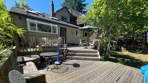 Une terrasse en bois avec des meubles d’extérieur, un espace salon couvert et une maison en arrière-plan.