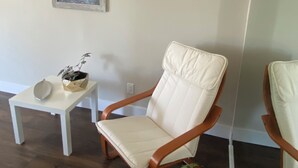 Une pièce avec une chaise blanche, une petite table blanche ornée d’une plante et un tableau encadré accroché au mur.