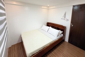 A single bed with a wooden frame, white bedding, and a wooden floor.